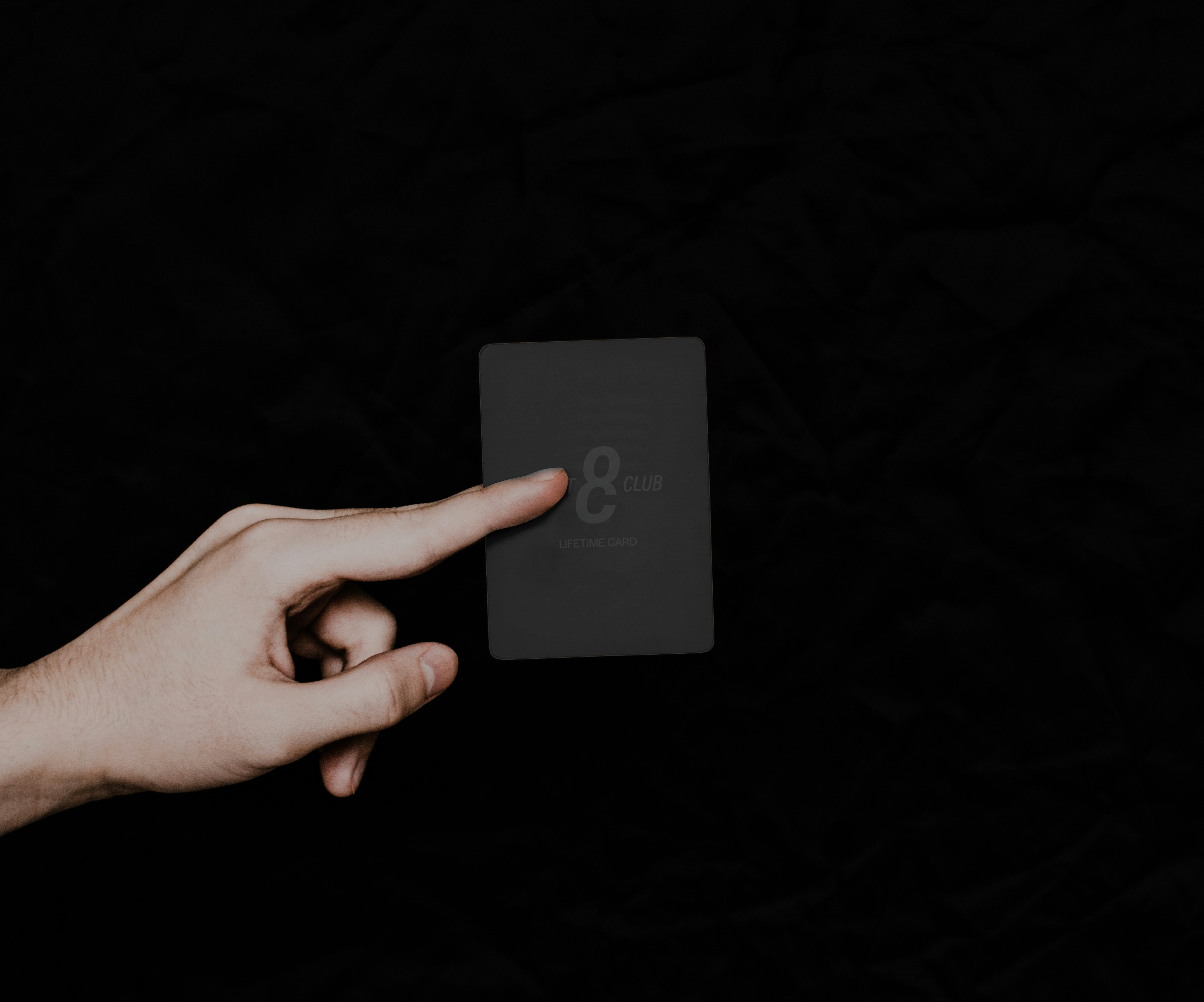 A hand presenting the matte black 8CLUB Lifetime Card